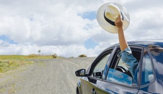 a passenger holding a hat outside the window of a car while having a roadtrip