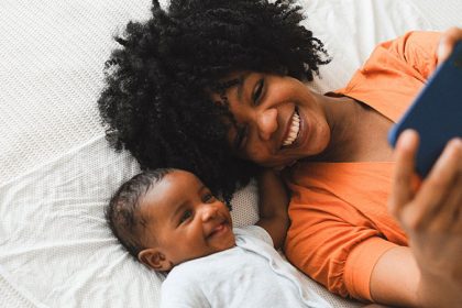 black woman with afro hairstyle taking selfie with a baby while lying on the bed
