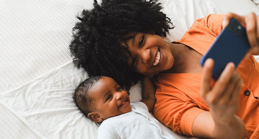 black woman with afro hairstyle taking selfie with a baby while lying on the bed